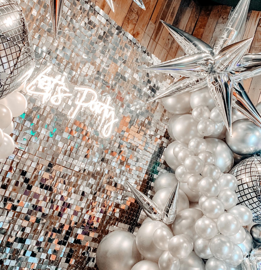 Silver Shimmer Wall Photo Backdrop draped with Balloon Garland for holiday party with a neon sign. 